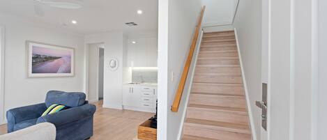 Una sala de estar moderna con un sofá azul, una escalera de madera y una zona de cocina.