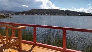 A wooden deck with a red railing overlooking a calm lake with distant hills. - Titicaca Kontiki lodge, culture, landscapes and nature for families and couples, (Puno)