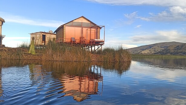 A houseboat with a deck and chairs, surrounded by water and vegetation. - Titicaca Kontiki lodge, culture, landscapes and nature for families and couples, (Puno)