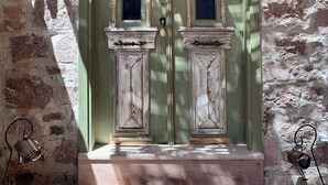 A rustic stone building with a green door featuring two windows, a small porch, and a metal bell. - Lalekar Butik Otel (Ayvalik)