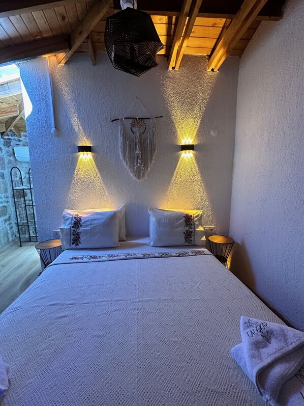 Une chambre confortable avec un grand lit, deux lampes fixées au mur et une décoration en macramé au-dessus du lit.