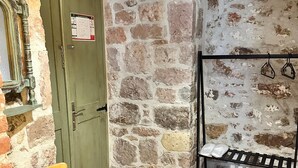 A rustic room with exposed brick walls, a green door, a wooden chair, and a metal rack with shoes. - Lalekar Butik Otel (Ayvalik)