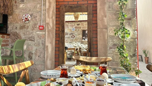 An outdoor dining area with a brick wall, a thatched roof, and a view of a courtyard. - Lalekar Butik Otel (Ayvalik)