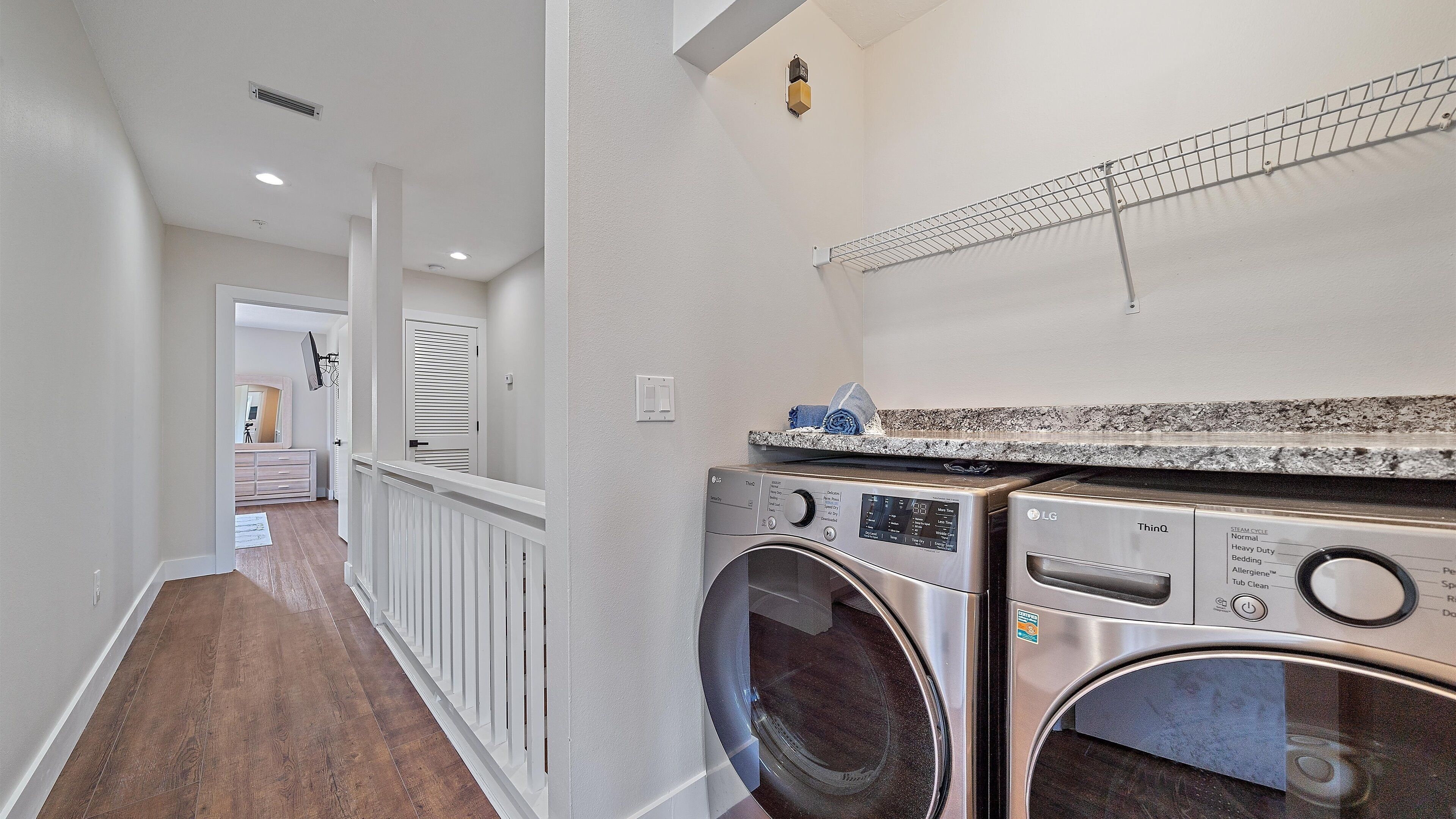 A laundry area with two front-loading washers, a metal drying rack, and a white door leading to another room.