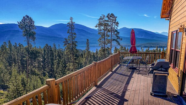 A hot tub on a wooden deck with a view of mountains and trees.