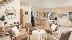 A spacious living area with a round wooden coffee table, comfortable seating, a large mirror, and a view of the kitchen in the background.