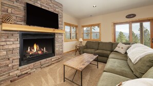 A living room with a fireplace, a flat-screen TV mounted above it, a green sofa, and a wooden coffee table.