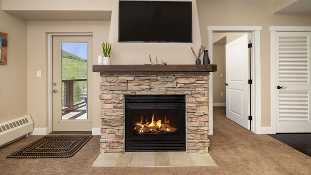 A living room with a stone fireplace, a mounted TV, and a door leading outside. - Base Camp 313 1 Bedroom Condo by RedAwning (Granby)