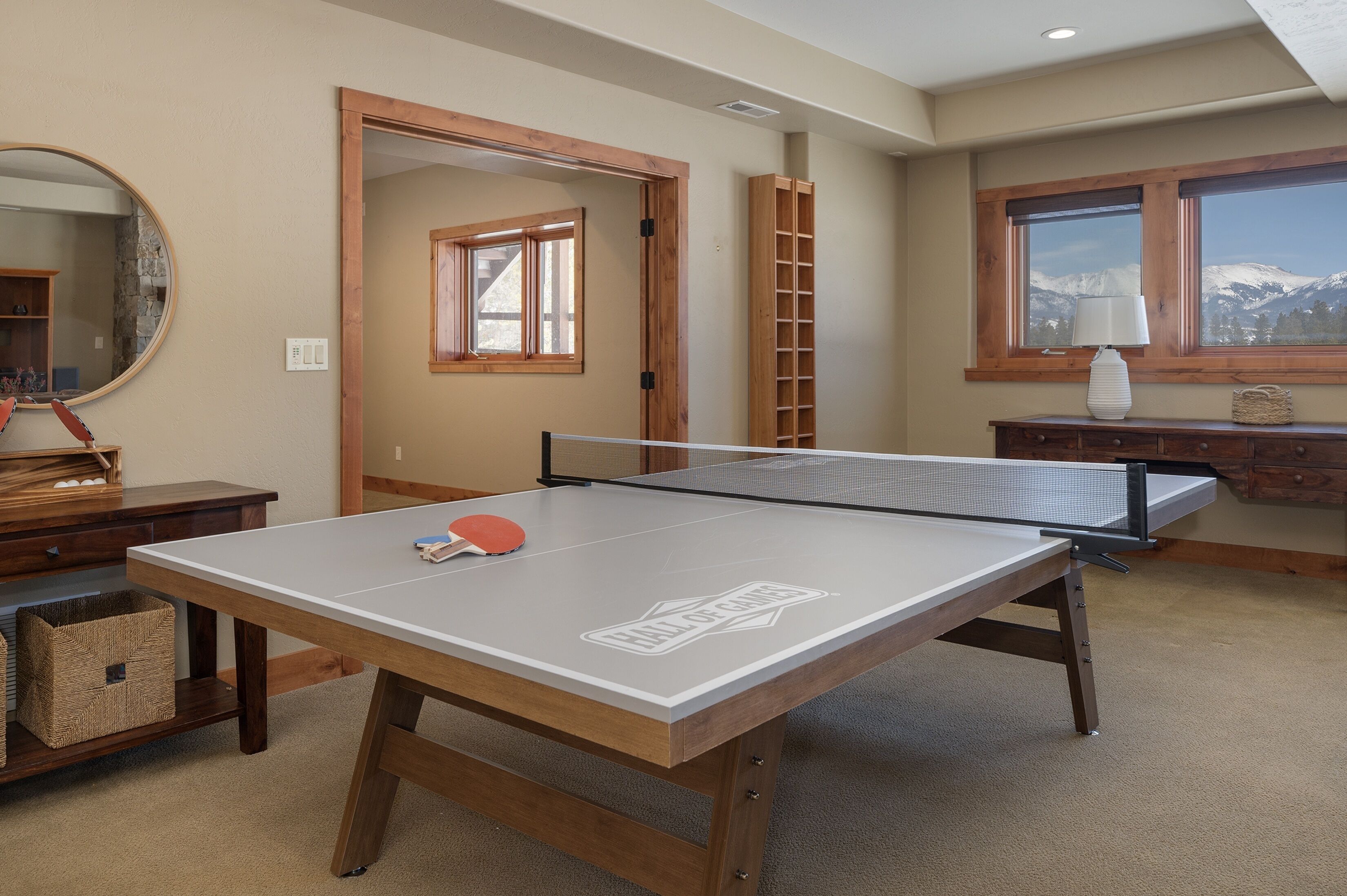 A ping pong table in a room with a wooden floor, a mirror, and a window with a view of mountains.