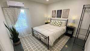 A bedroom with a bed, bedside tables, a radiator, a potted plant, a patterned rug, and artwork on the wall.