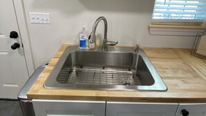 A kitchen with a stainless steel sink, wooden countertop, and a window with blinds.