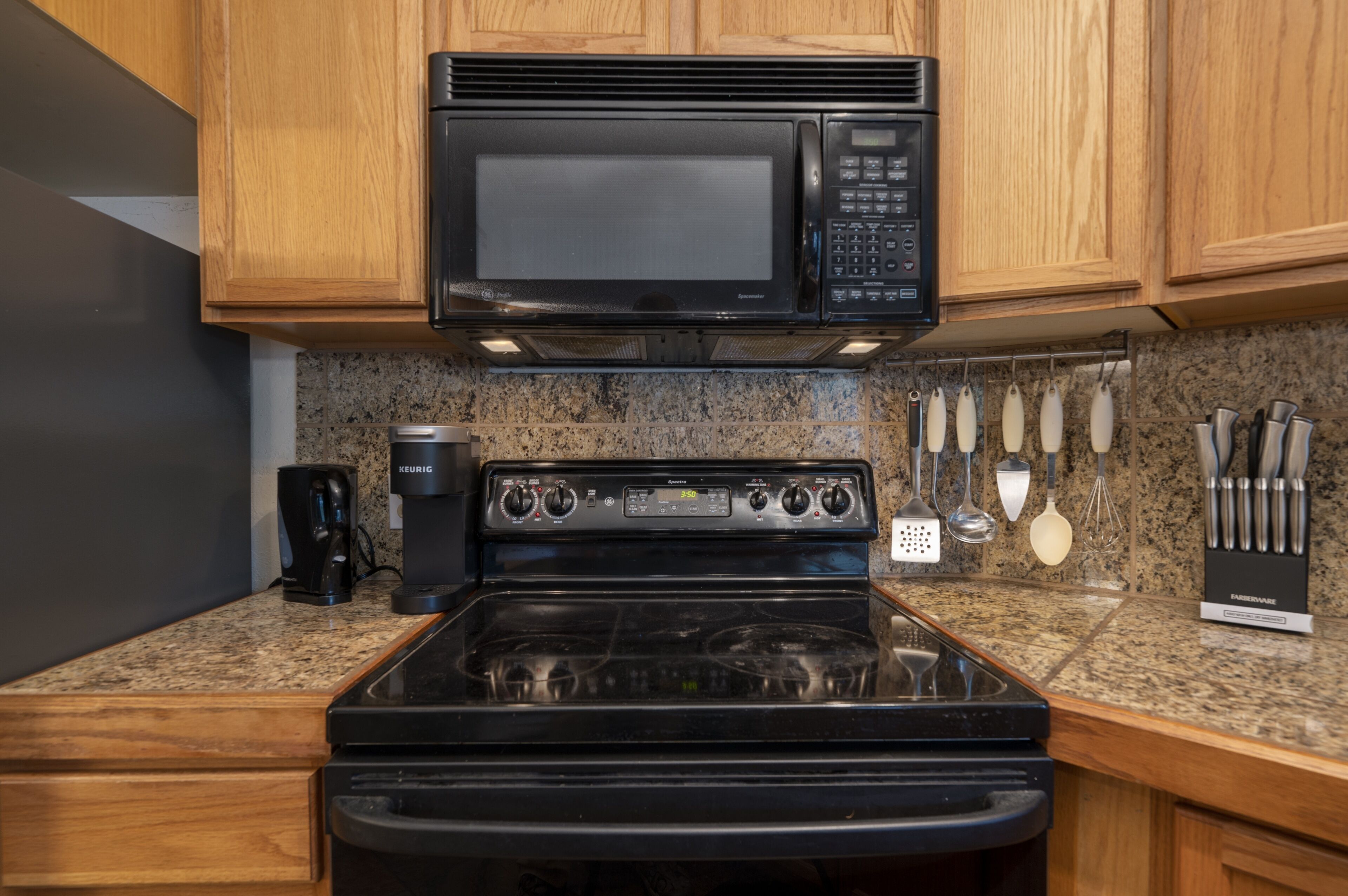 A kitchen with a black microwave, stove, and coffee maker.