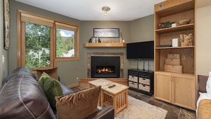 A cozy living room with a fireplace, a leather sofa, a wooden coffee table, and a bookshelf. - Iron Horse C4093 Condo by RedAwning (Winter Park)