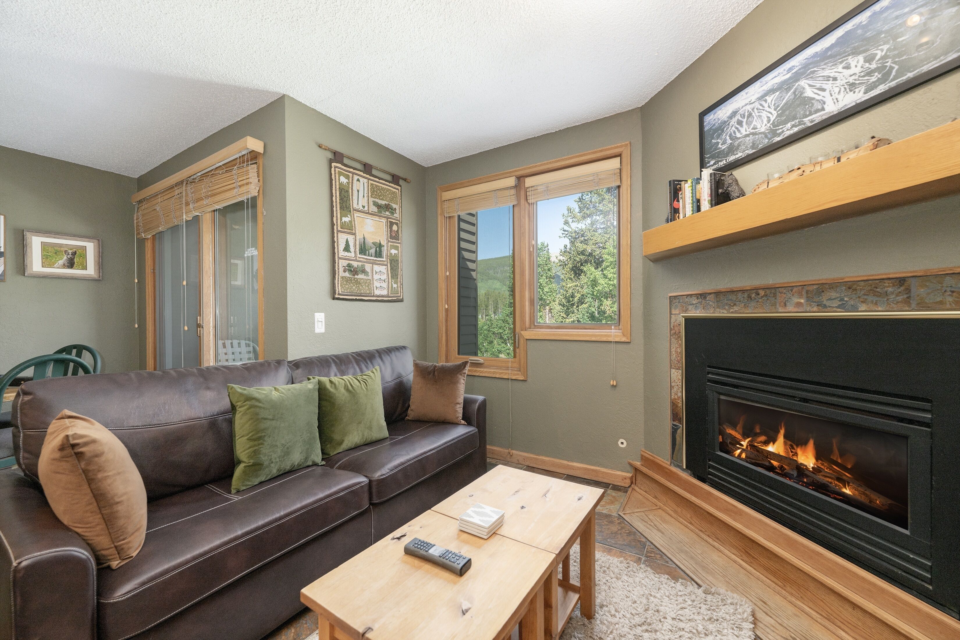 A living room with a fireplace, a leather sofa, a coffee table, and a window with blinds.