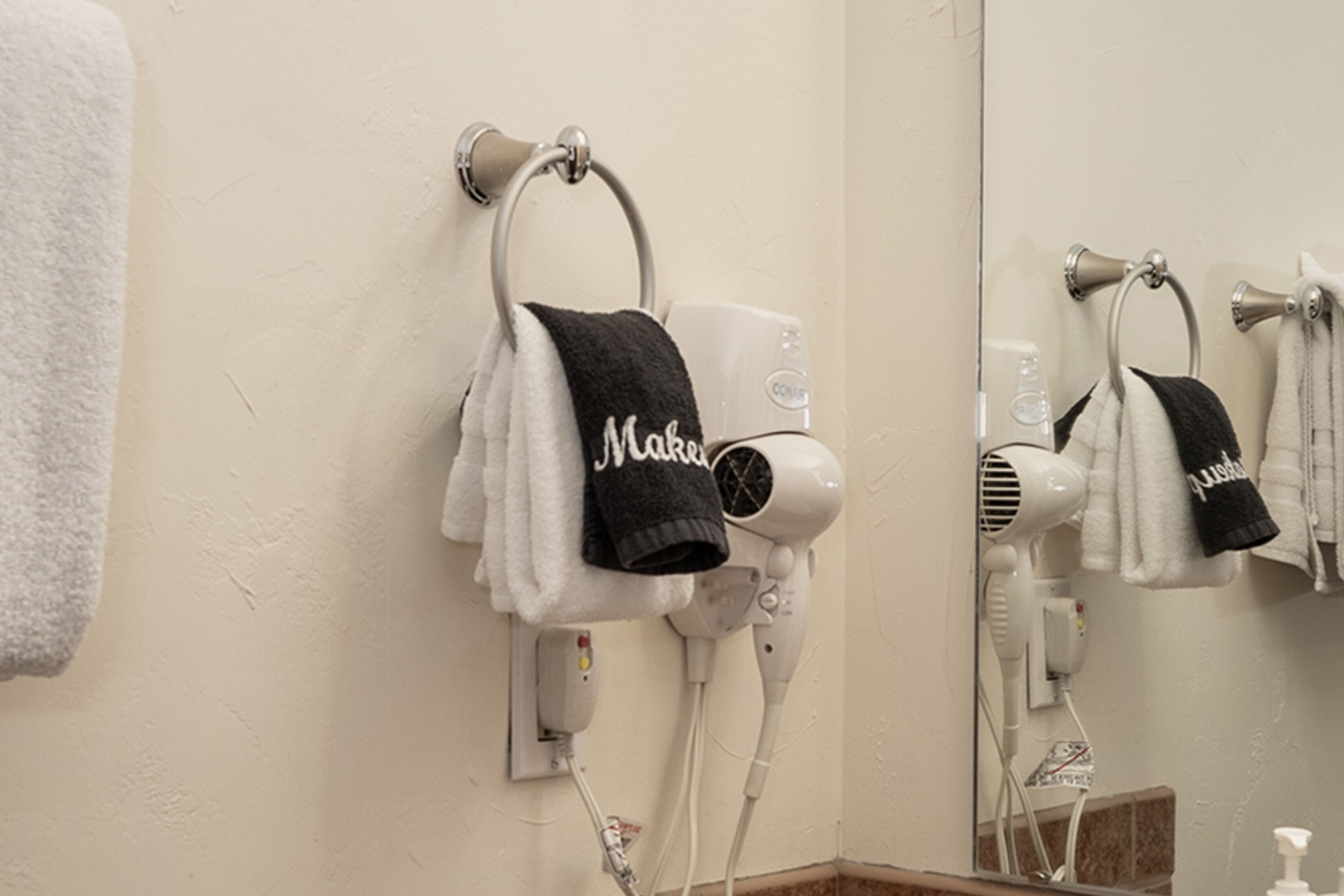 A bathroom with a hairdryer mounted on the wall, a towel rack with a black towel, and a mirror reflecting the hairdryer and towel.