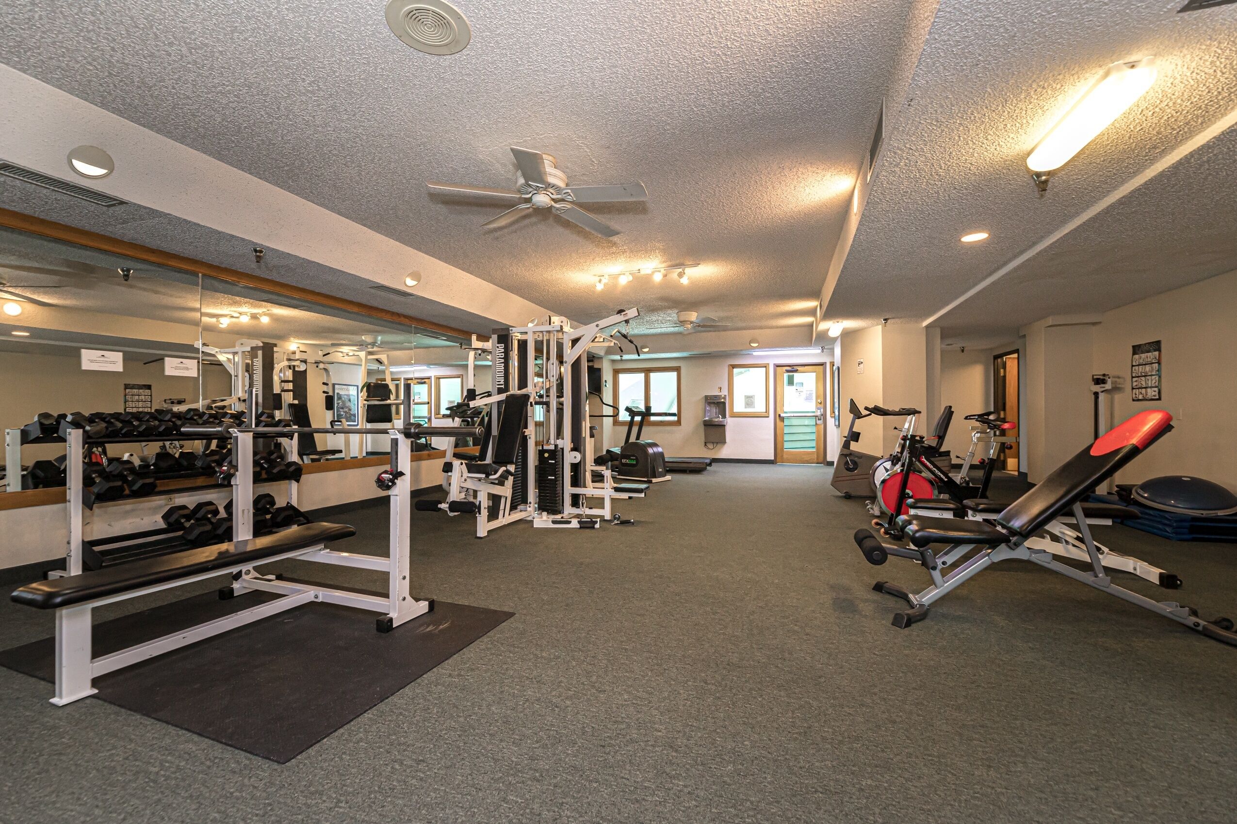 A gym with various exercise equipment, mirrors, and a ceiling fan.