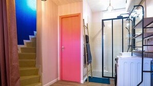 Una escalera con una puerta rosa, un área de lavandería con lavadora y una zona de ducha con puerta de vidrio.