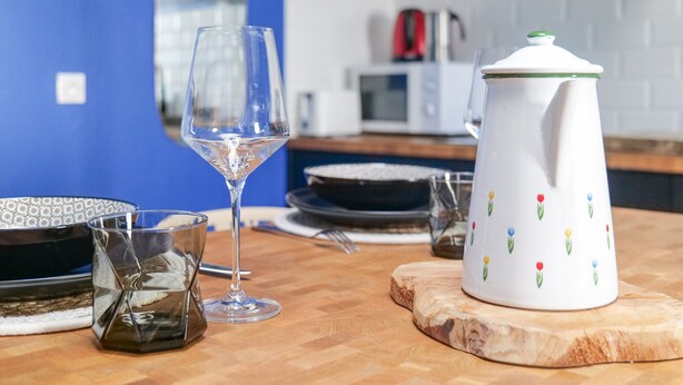 Una cocina con pared azul, un hervidor blanco, un vaso y un plato sobre una tabla de madera.