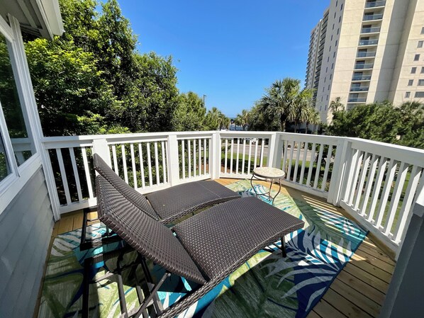 Eine Terrasse mit Tisch und Stühlen, umgeben von einem weißen Geländer, mit Blick auf ein Wohngebiet mit Bäumen und Häusern.