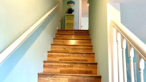 Een houten trap met witte balustrades, leidend naar een plateau met een groene kast en een kleine plant.