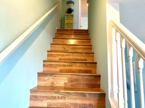 Una escalera de madera con balaustres blancos que lleva a un rellano con un armario verde y una planta pequeña.