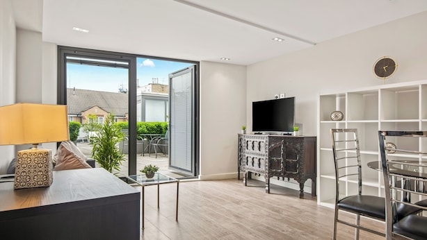 A modern living room with a glass table, a sofa, a TV, and a bookshelf. - Chic and Modern Flats in Hoxton, Shoreditch (London)