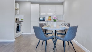 A modern kitchen with white cabinets, a dining table with four chairs, and a small island with a microwave. - Chic and Modern Flats in Hoxton, Shoreditch (London)
