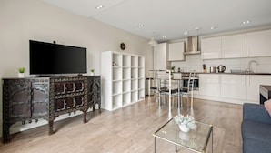 A modern living room with a flat-screen TV, a decorative cabinet, a glass coffee table, and a sofa. - Chic and Modern Flats in Hoxton, Shoreditch (London)