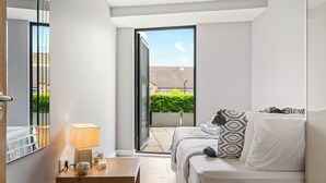 A modern bedroom with a bed, bedside table, lamp, and a view of the outside. - Chic and Modern Flats in Hoxton, Shoreditch (London)