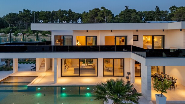 Uma casa moderna de dois andares com piscina, janelas amplas e área de estar externa.