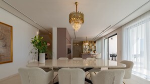 Uma sala de jantar moderna com uma mesa grande, cadeiras brancas e um lustre.