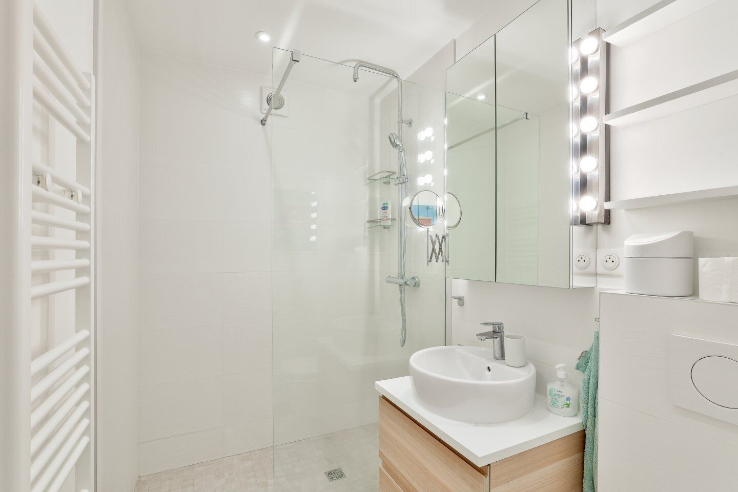 A modern bathroom with a glass-enclosed shower, a vanity with a sink, and a mirror with lights.