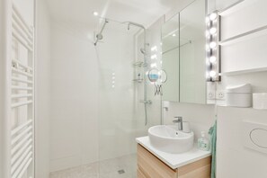Une salle de bain moderne dotée d’une douche à parois de verre, d’un meuble-lavabo et d’un miroir avec éclairage intégré.