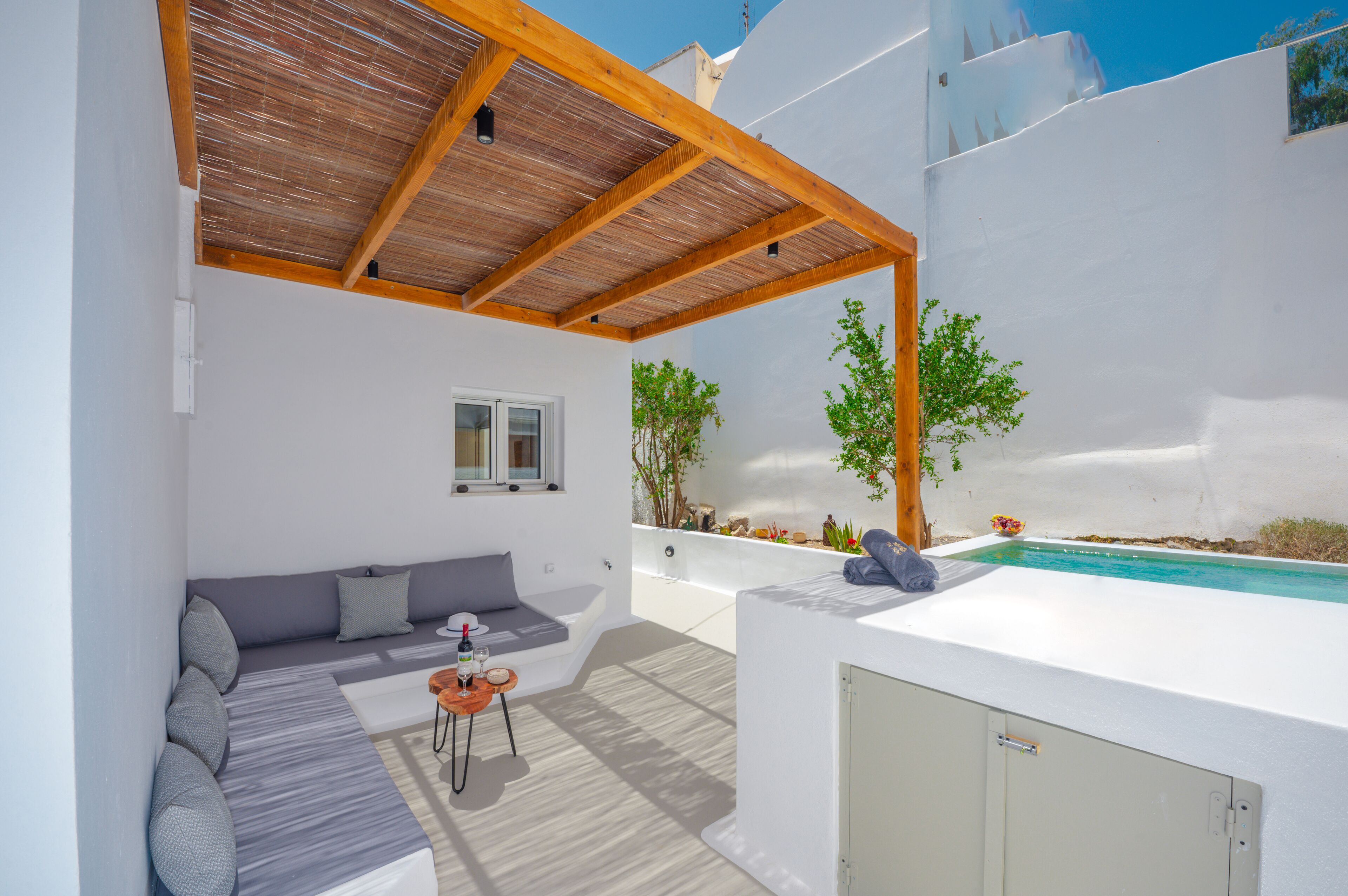 Un'area relax esterna moderna con piscina, una pergola in legno e un muro bianco.