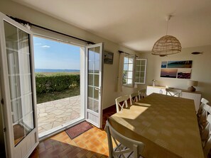 Ein Essbereich mit großem Tisch, Stühlen und Meerblick durch offene Türen.