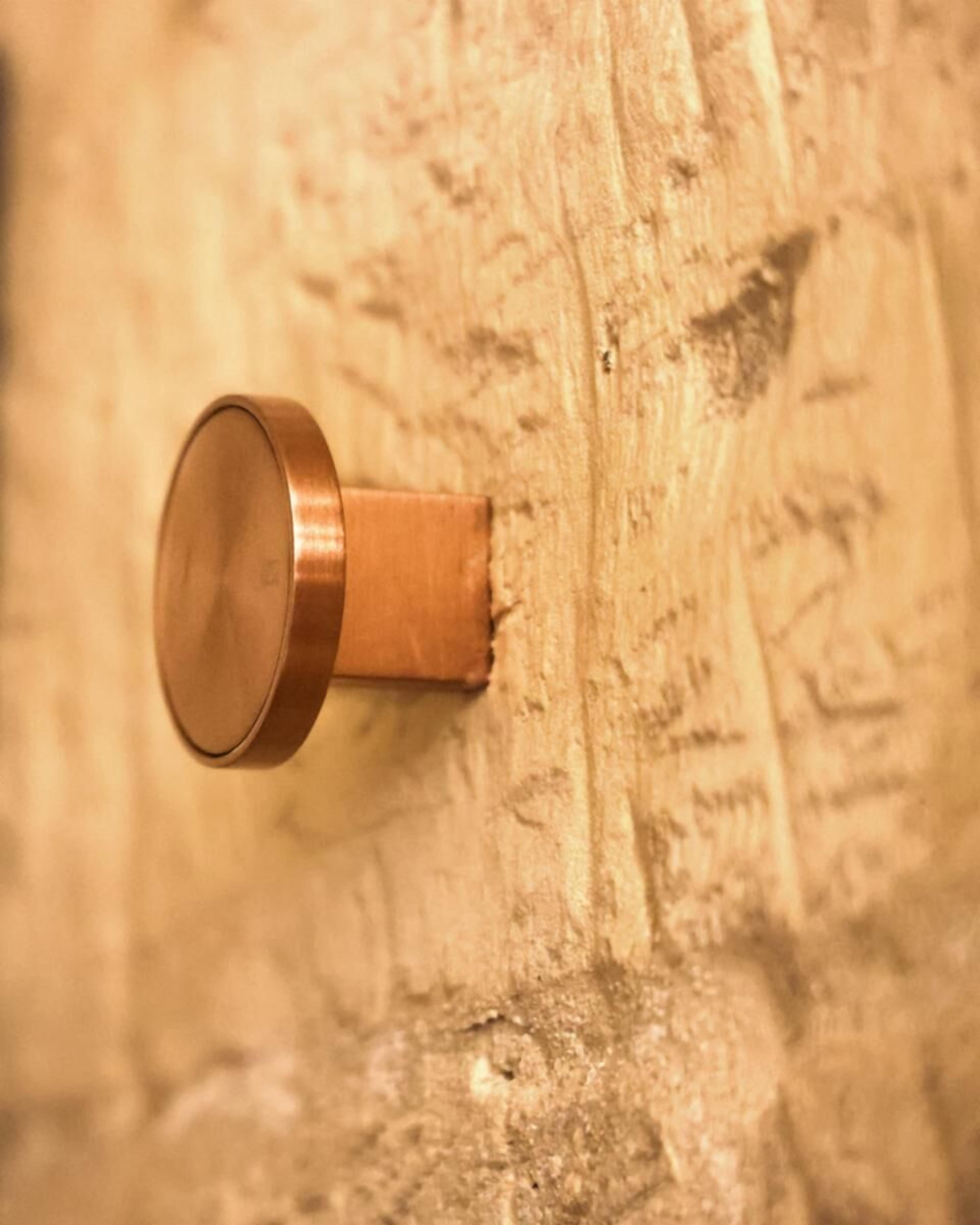 Een close-up van een metalen voorwerp, mogelijk een deurklink, bevestigd aan een houten oppervlak met duidelijke nerf en textuur.