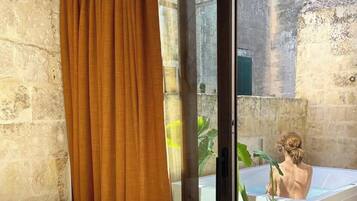 A room with a sliding glass door leading to an outdoor area, a bathtub, and a potted plant.