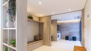A modern, well-lit room with a built-in bench, shelving with plants, and a laundry area with a washing machine and drying rack. - 360 Ambience Vila Mariana (São Paulo)