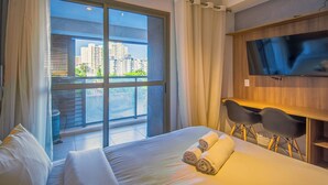 A hotel room with a large window, a bed, a desk with a chair, and a flat-screen TV mounted on the wall. - 360 Ambience Vila Mariana (São Paulo)