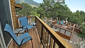 Une terrasse en bois avec des chaises bleues et une petite table, d’où l’on peut admirer un paysage montagneux.