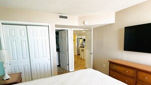 Een slaapkamer met een bed, een kapstok, een spiegel en een deur naar een keuken.