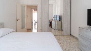 Quarto de hotel com cama, guarda-roupa, televisão e casa de banho visível através de uma porta.