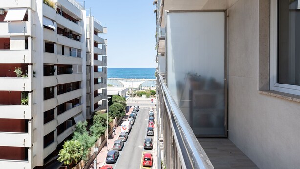 Edifício alto com várias varandas, vista para uma rua movimentada e um corpo de água.
