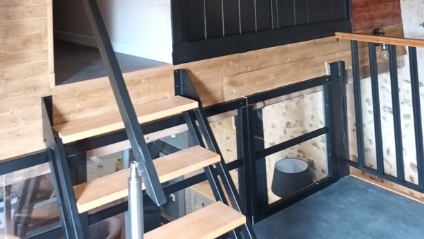 A modern interior with a wooden staircase, black railings, and a climbing wall.