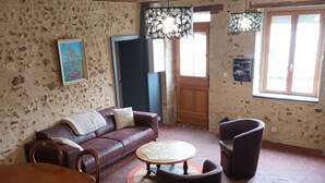 A rustic living room with a wooden ceiling, a brown leather sofa, a round coffee table, and a dining table with chairs.