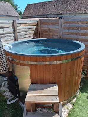 A wooden hot tub with a metal frame, surrounded by a wooden fence, and a grill unit to its left.