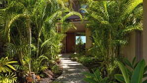 A pathway flanked by lush tropical plants leading to a building entrance. - Elevated 2BR Hillside Villa 4102 at Hualalai – Ocean Views & Island Lifestyle (Kailua Kona)
