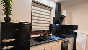 A modern kitchen with a black refrigerator, white cabinets, a stove, and a window with blinds. - Hearty vacation apartment with a warm ambience in a private location (Delmenhorst)