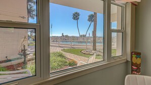 A view from a window with a view of a pool, palm trees, and a fence. - Directly on the Gulf - Unit  6 - 1 Bedroom - Ground Floor - Sleeps 4 (Venice)
