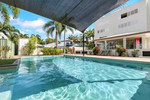 Una piscina con zona ombreggiata, circondata da palme e un edificio con il cartello Coca-Cola.